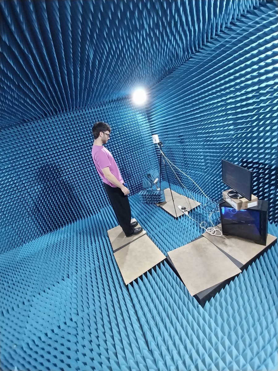 A volunteer standing in a blue anechoic chamber in front of a radar on a tripod, with a second radar and the acquisition computer nearby