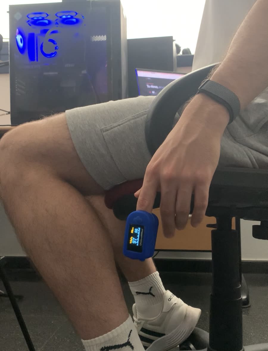 A seated volunteer wearing a blue finger pulse oximeter that shows a pulse of 66