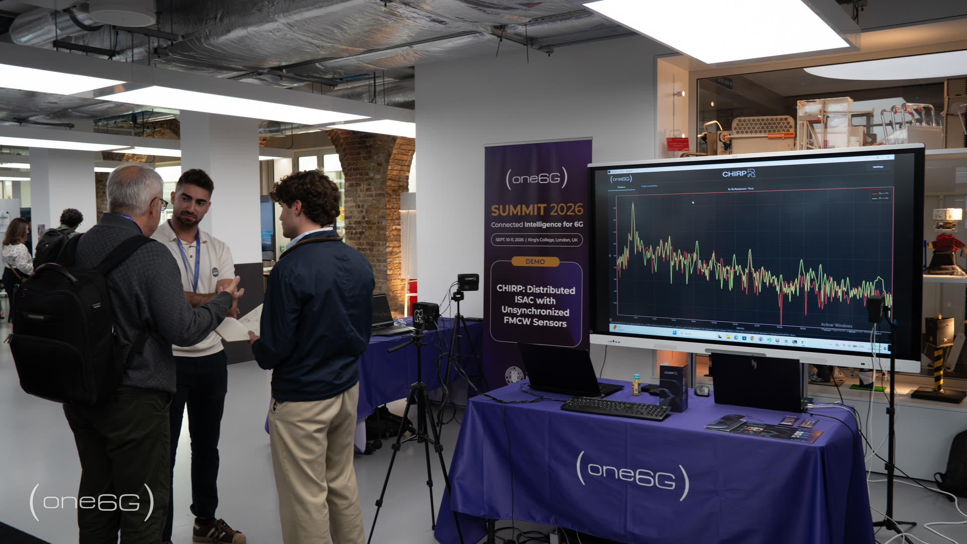 The CHIRP demonstration booth at the one6G Summit 2026, with a large screen showing live sensing traces and FMCW sensors mounted on tripods