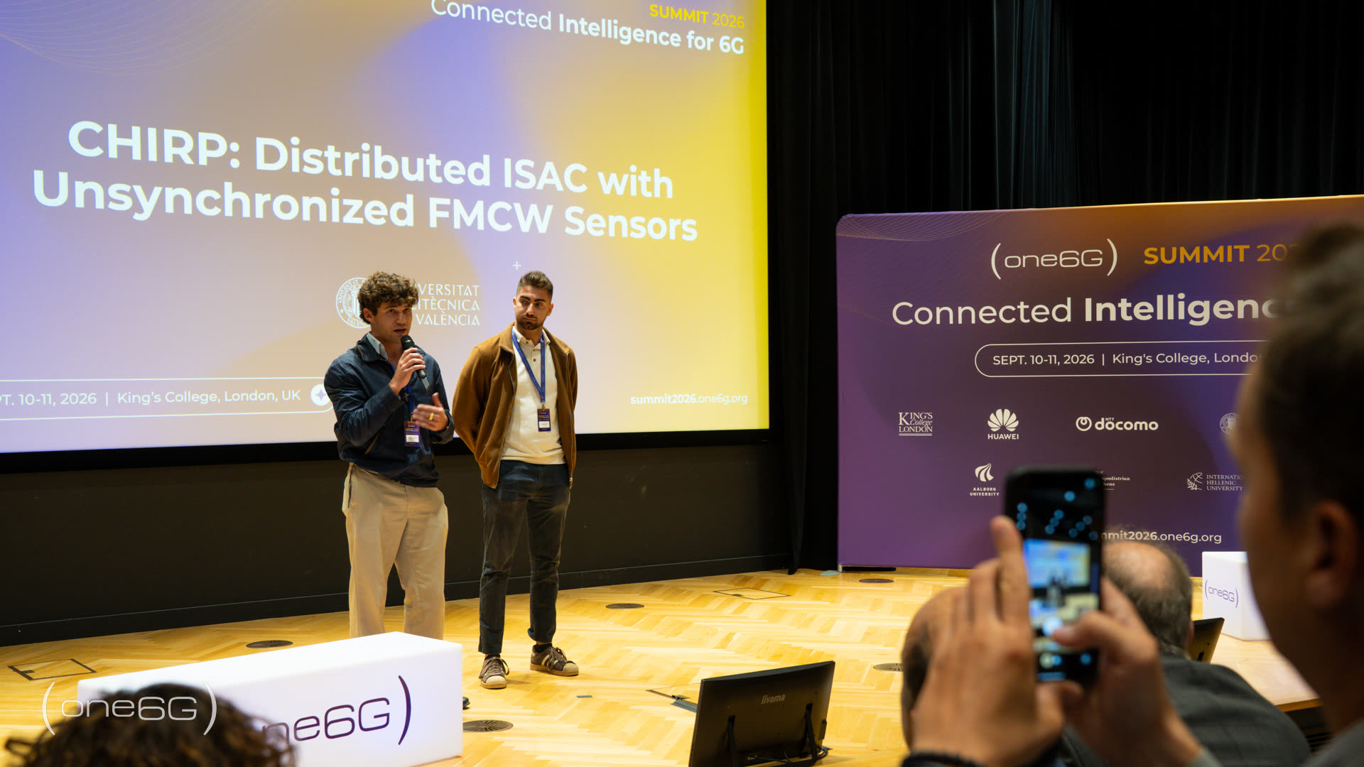 Two CHIRP team members presenting “CHIRP: Distributed ISAC with Unsynchronized FMCW Sensors” on stage at the one6G Summit 2026, King's College London