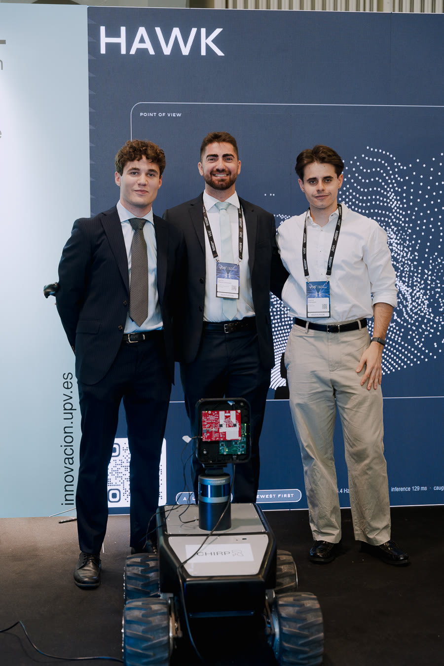 Three members of the CHIRP team standing behind the HAWK rover, in front of the HAWK display